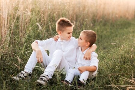 Brothers wearing white clothes sitting on the grass while looking at each other