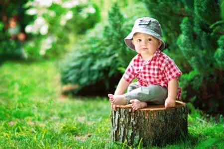 Adorable little boy sitting on tree stump in the garden