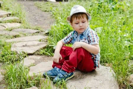 Cute handsome little boy wearing hat and red jeans sitting on the rock in the lawn