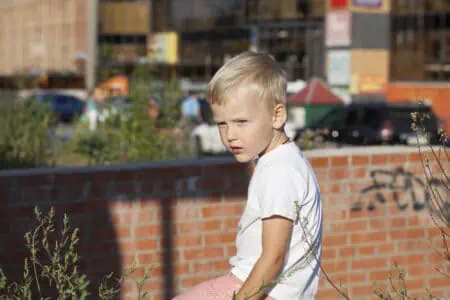 Handsome blonde little boy in a white shirt walking in the street