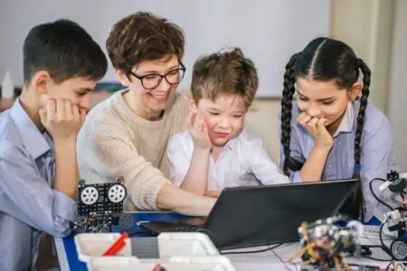 Kids with their mother learning programming using laptop at home with robots in front of them