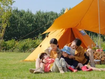Happy family of four in front of camping tent in the park
