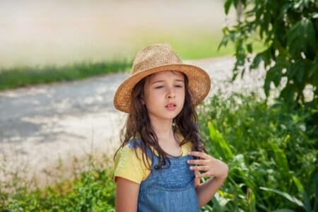 Beautiful young girl in straw hat standing in the park during hot season