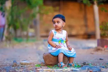 Indian little girl wearing dress sitting on a rock outdoors
