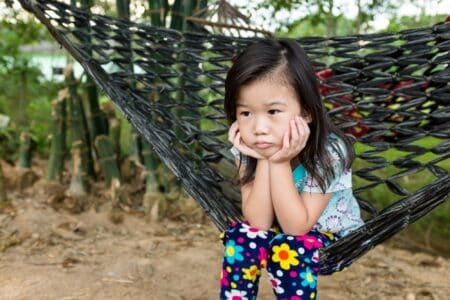 Unhappy girl propping up her face and sitting alone in hammock