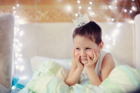 Handsome little prince wearing a crown lying in bed