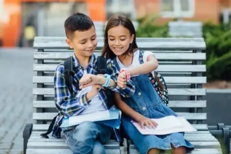 Young boy and girl looking at their smart watch while sitting on the bench