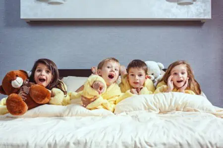 Adorable children in yellow pajama holding their teddy bear while lying on top of the bed in the bedroom