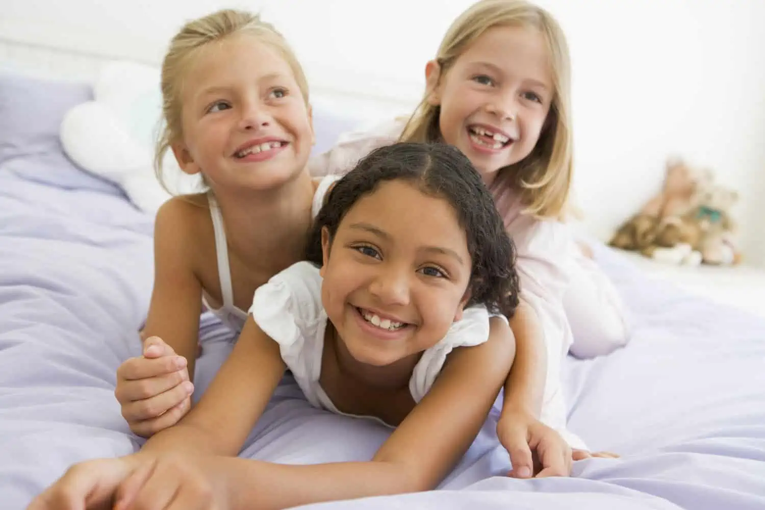 Three young girls lying on top of each other in their pajamas