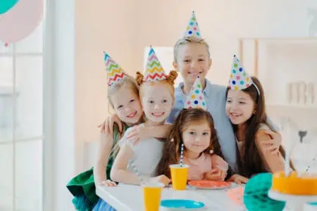 Five cheerful children wearing festive cone caps celebrating birthday together