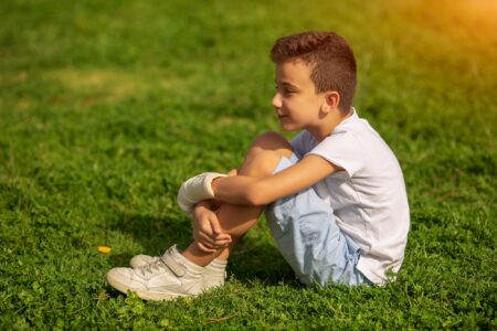 Brazilian young boy with cast sitting on the grass outdoors