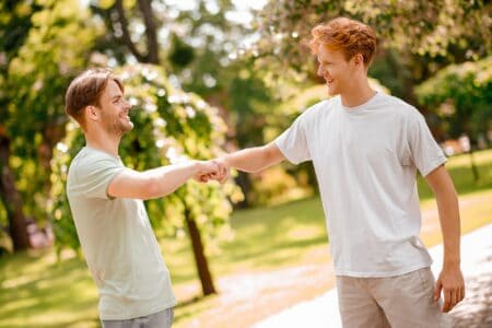 Two smiling grown men doing fist bump in the park on fine sunny day