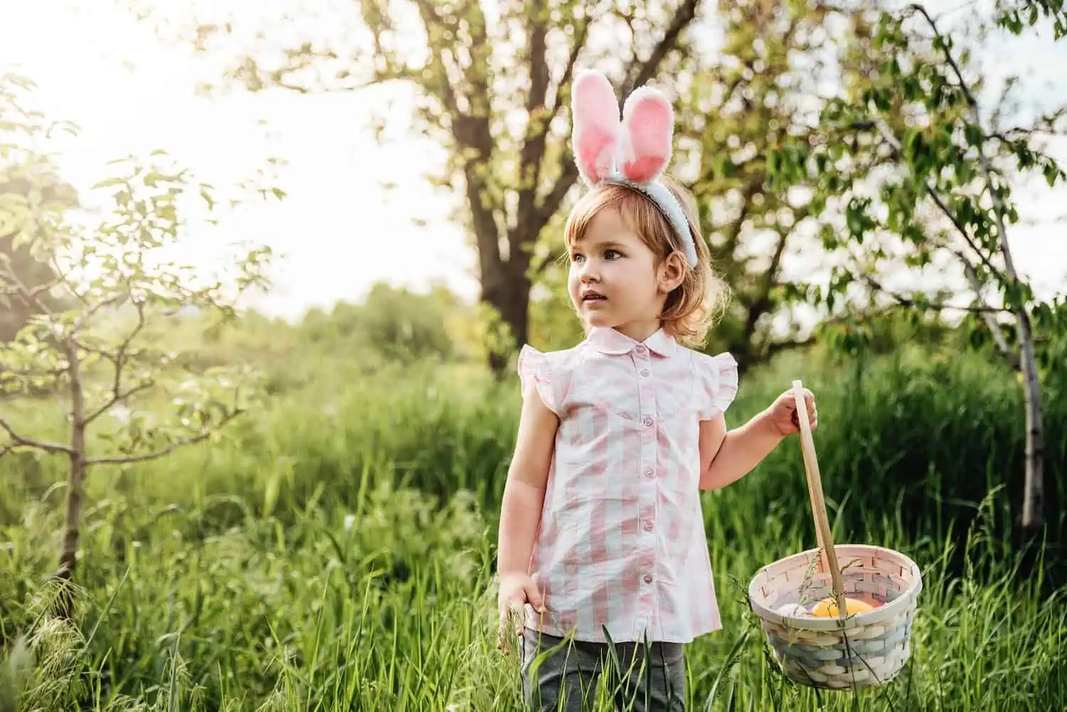 Little girl wearing bunny headband holding basket full of colorful easter eggs