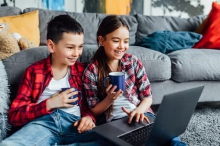 Brother and sister watching movie on laptop with cup of juice