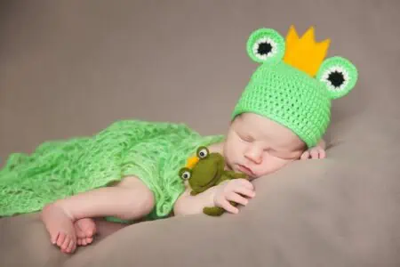 Cute newborn baby in frog costume with plush toy frog sleeping tightly on the bed
