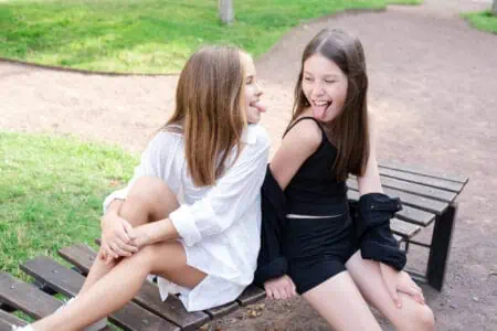 Funny sisters sitting on bench at the park teasing each other