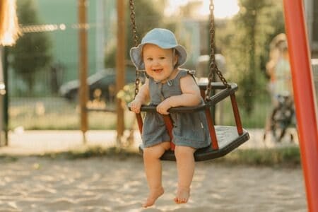 Cheerful toddler baby girl having fun on swing in the playground