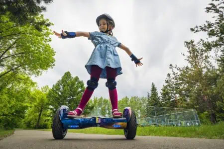 Little girl riding hoverboard in the park with safety gear