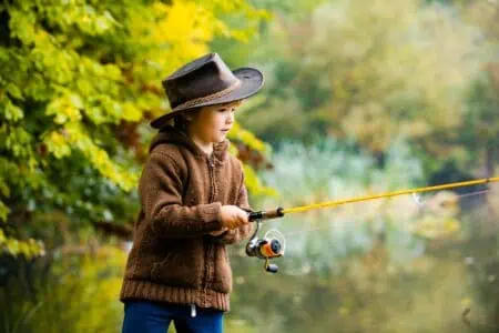 Adorable young boy wearing hat fishing by mountain lake in autumn