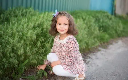 Beautiful little girl sitting near green grass outdoors