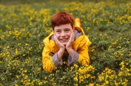 Scottish cheerful boy in yellow raincoat lying in blooming field