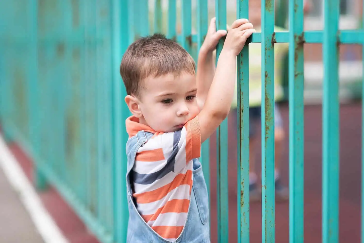 Cure little boy standing near the fence