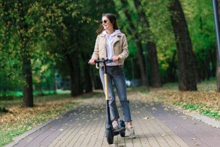 Young woman wearing sunglasses riding an electric scooter in autumn park