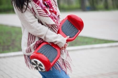 Woman holding modern red hoverboard in hands while walking in the park