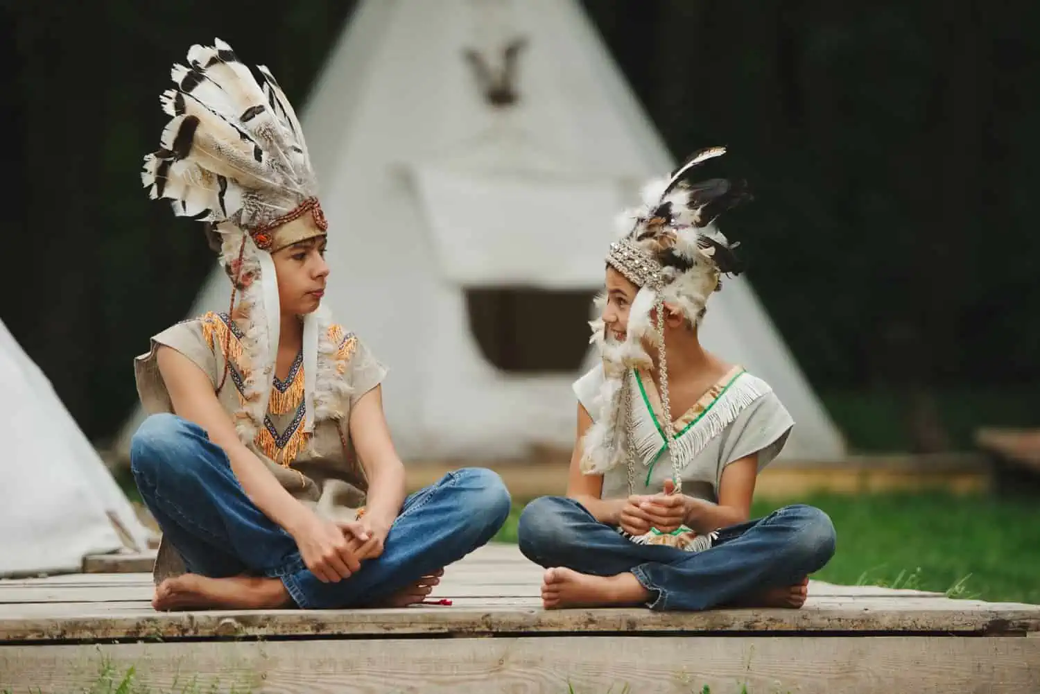 Two brothers in native american attire looking at each other while sitting outdoors