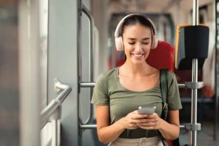 Smiling woman passenger wearing headphones listening to music while sitting in modern train