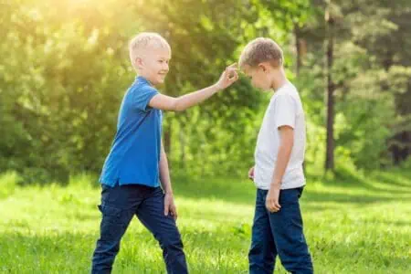 Blond boy click his finger on the forehead of his friend in a sunny park