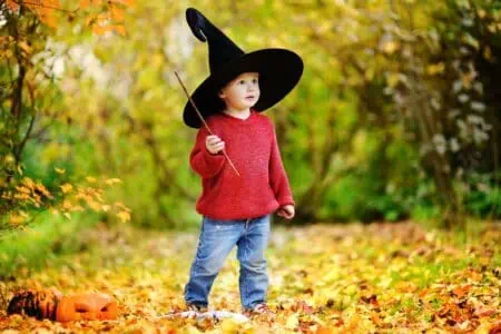 Adorable little wizard with hat playing with magic wand at autumn park
