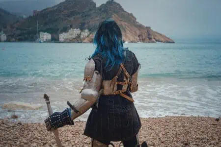 Girl in paladin costume with sword standing at the beach