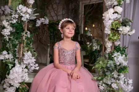 Adorable little girl in pink dress sits among flowers