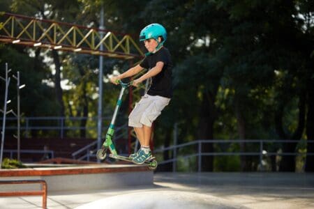 Young boy wearing helmet doing scooter tricks at the park