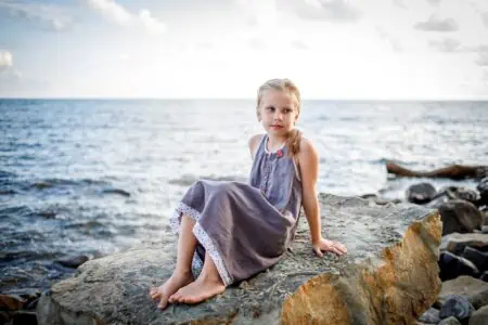 Swedish little girl in dress sitting on rock at the beach
