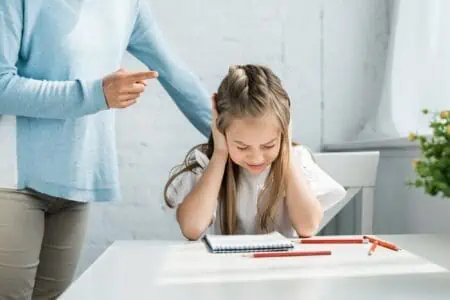 Young girl covering her ears while being scolded by her parent