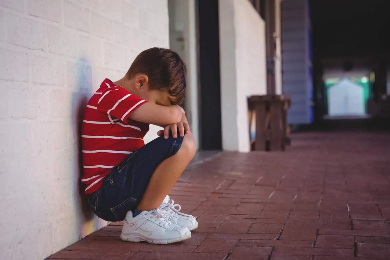 Abandoned boy crouching by wall at school building