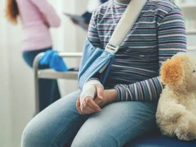 Child with arm brace and teddy bear sitting on bed at the clinic