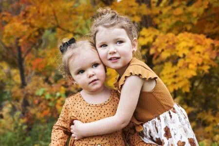 Two little sisters hugging each other on autumn park