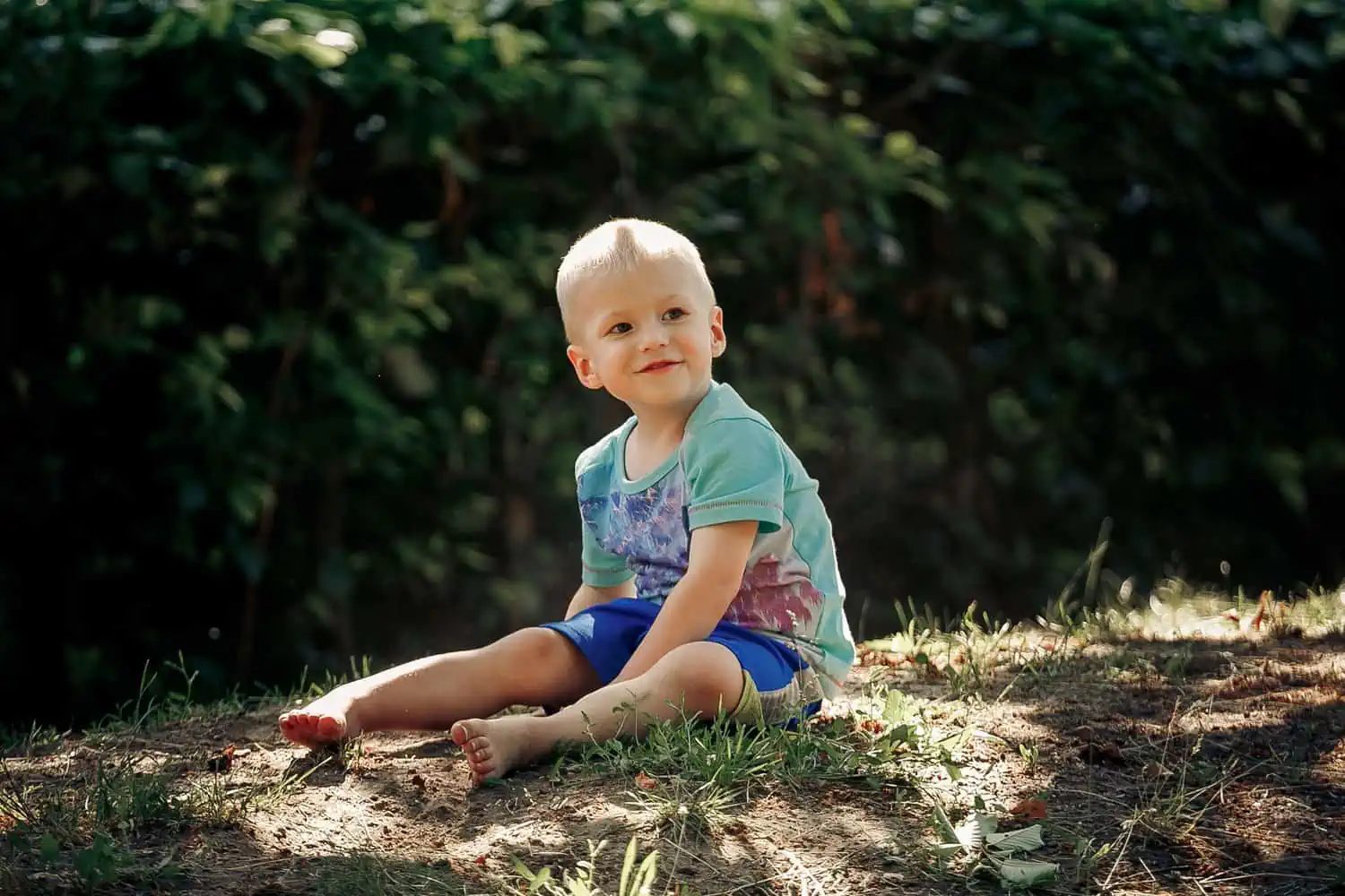 Barefoot adorable boy sitting on sand in the garden