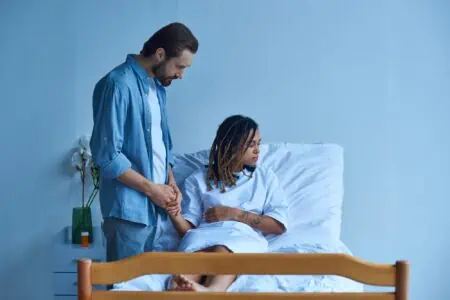 Sad woman resting on hospital bed being comforted by her husband
