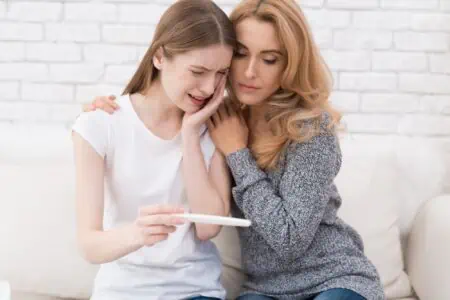 Teen girl holding a pregnancy test and being comforted by her mom