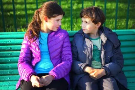 Siblings looking at each other while sitting on the bench in the park
