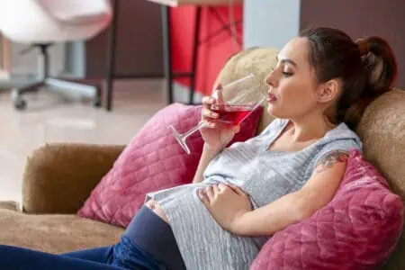Pregnant woman drinking alcohol while sitting on the couch at home