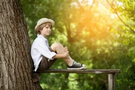 European young boy wearing stylish clothes sitting on a bench beside the tree