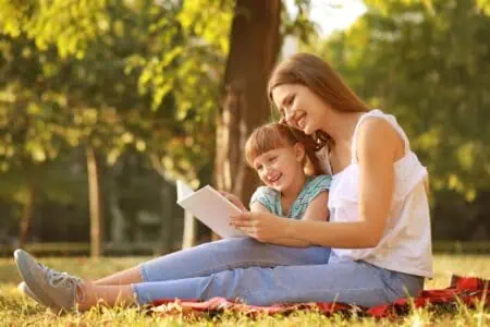 Mother and little daughter reading book in the park