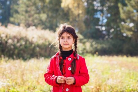 Adorable girl in red jacket standing in the meadow