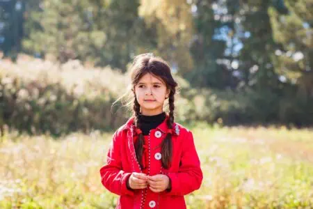 Adorable girl in red jacket standing in the meadow