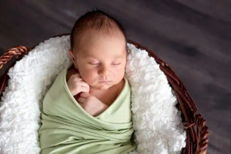 Cute newborn baby boy wrapped in green cloth sleeping in a basket